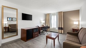 Une chambre d’hôtel avec un bureau en bois, un canapé, une télévision et un grand miroir.