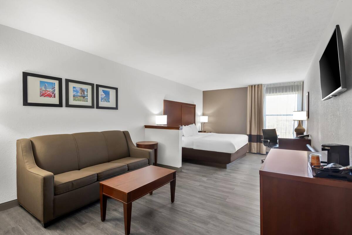 A hotel room with a sofa, a bed, a desk, a TV, and framed pictures on the wall.