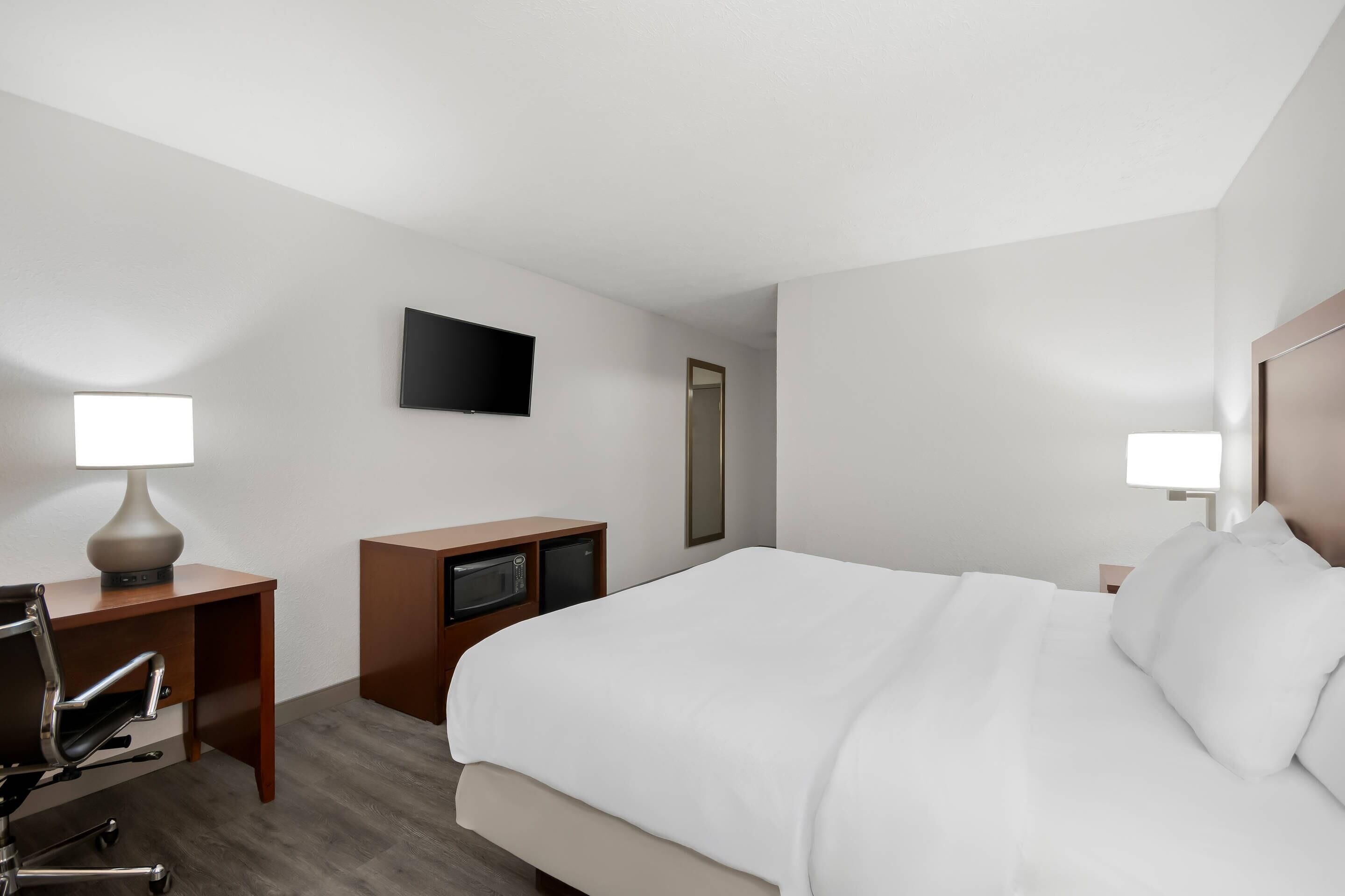 A hotel room with a bed, a desk with a lamp, a television, and a mirror.