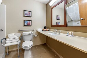 A bathroom with a toilet, sink, and a chair with wheels. There are framed pictures on the wall and a mirror above the sink. - Comfort Inn & Suites Cincinnati Eastgate (Cincinnati)