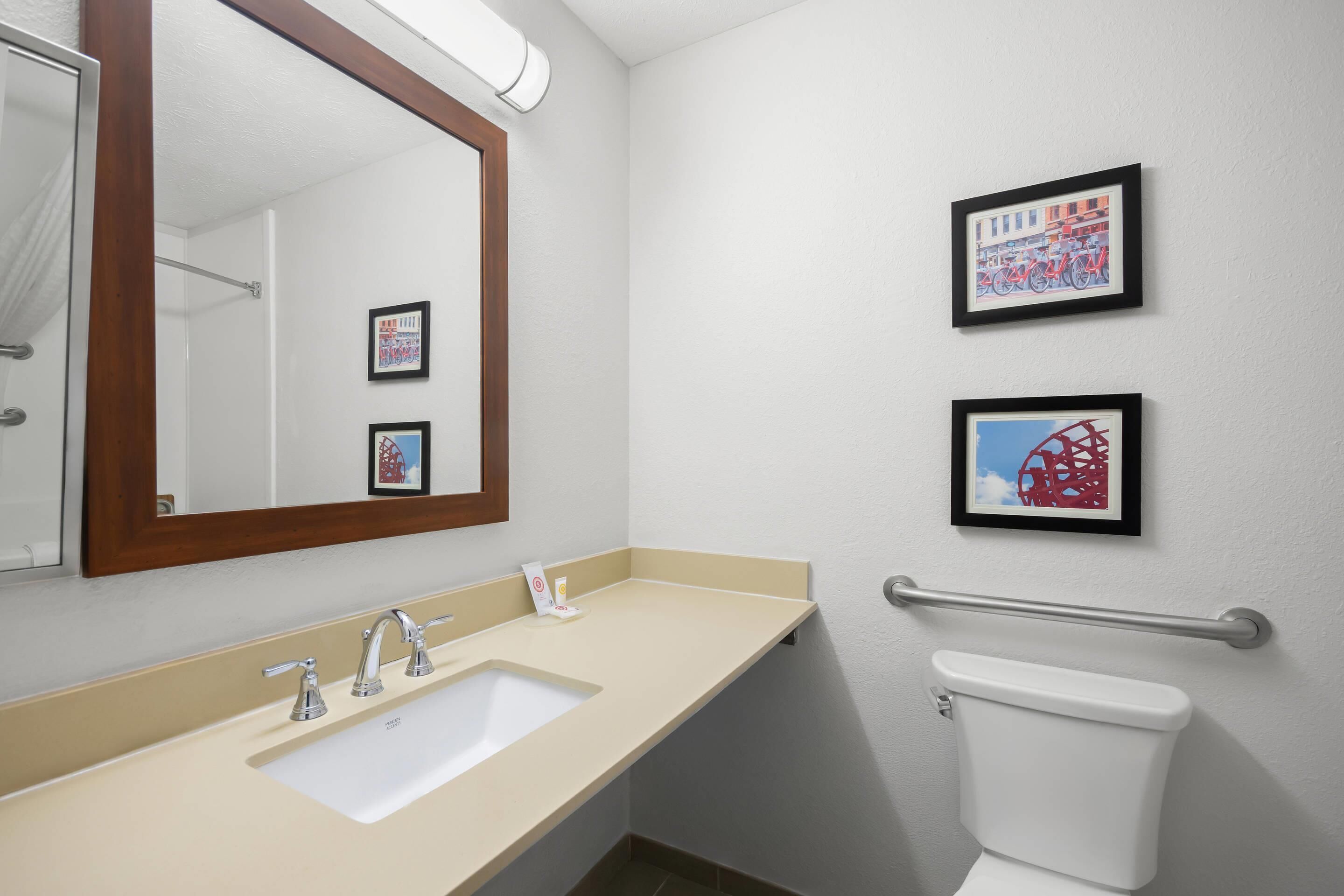 A bathroom with a sink, mirror, toilet, and two framed pictures on the wall.