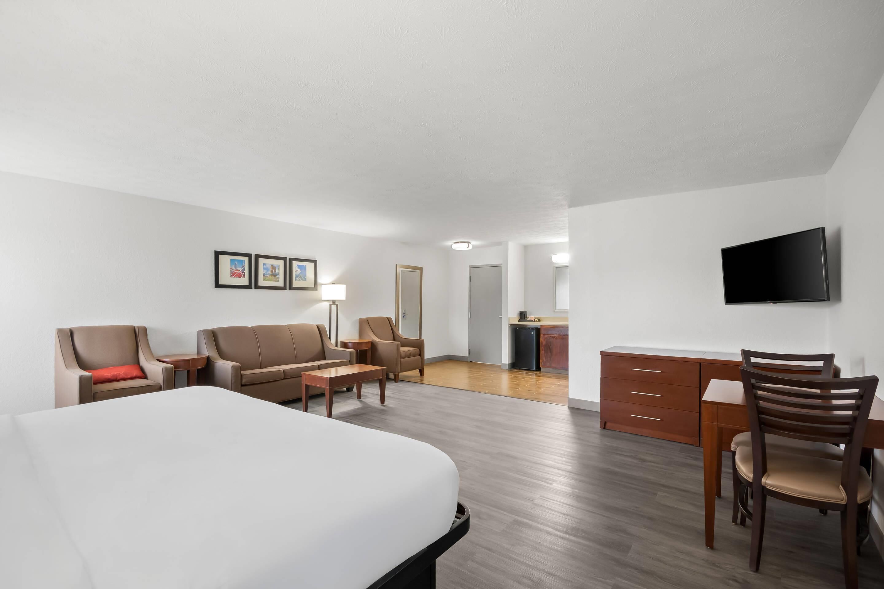 A hotel room with a large bed, a desk with a chair, a sofa, and a TV mounted on the wall.