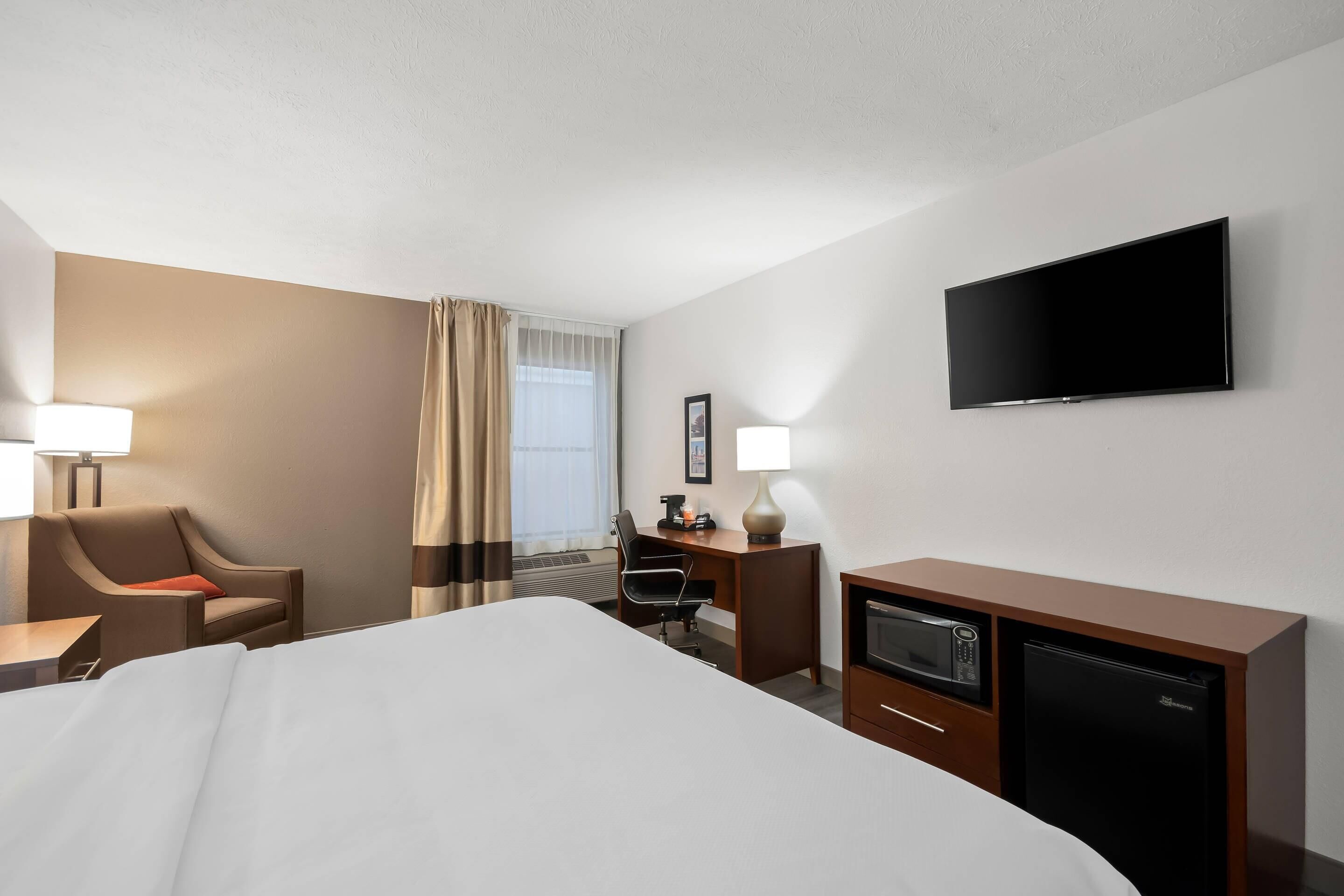 A hotel room with a bed, desk, chair, TV, and a microwave.