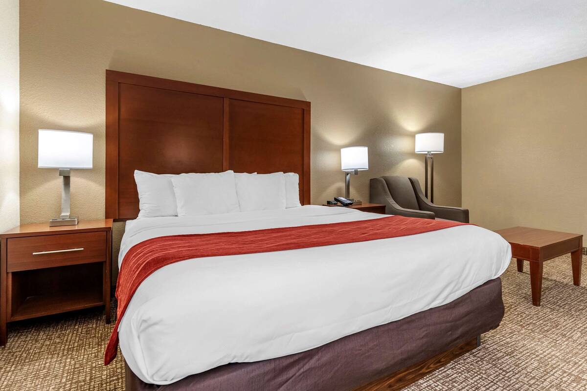 A hotel room with a large bed, two bedside tables, a chair, and two wall-mounted lamps.