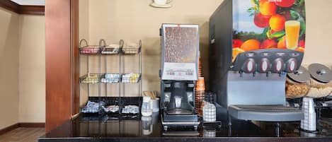 A coffee shop counter with a coffee machine, a juice dispenser, and a sign indicating it's open 24 hours.