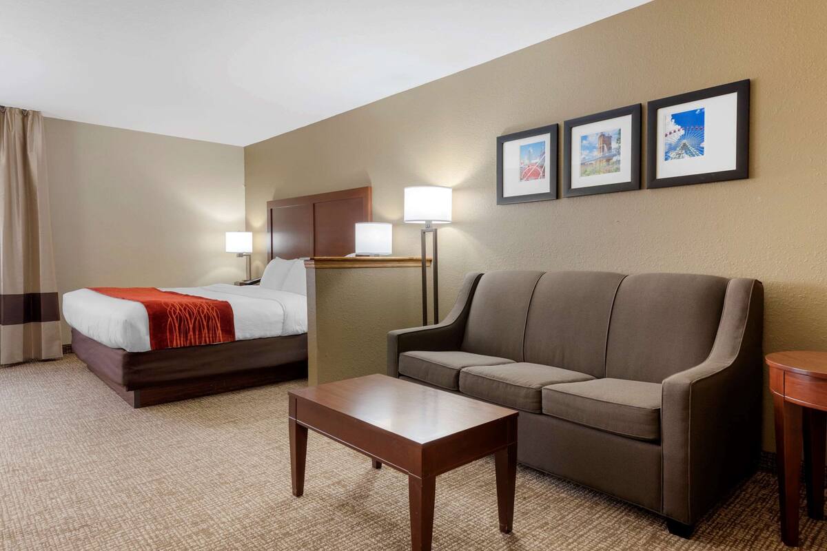 A hotel room with a bed, a sofa, a coffee table, and a lamp. There are three framed pictures on the wall.