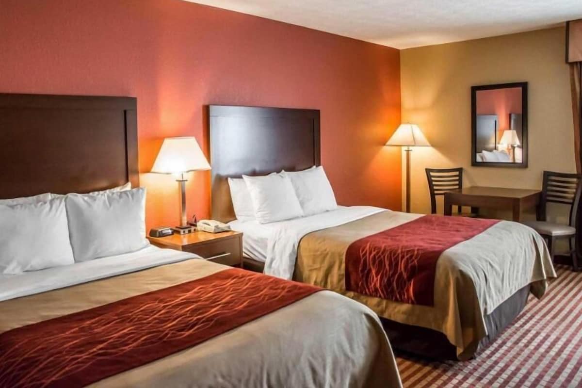 A hotel room with two beds, nightstands, lamps, a table, and chairs.