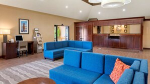 Un hall d’hôtel avec un canapé bleu, un comptoir d’accueil, un ordinateur et, au fond, un coin cuisine.