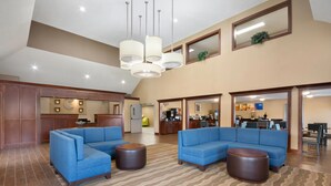 Un hall d’entrée spacieux, avec des canapés bleus, une moquette à motifs et un coin cuisine à l’arrière-plan.