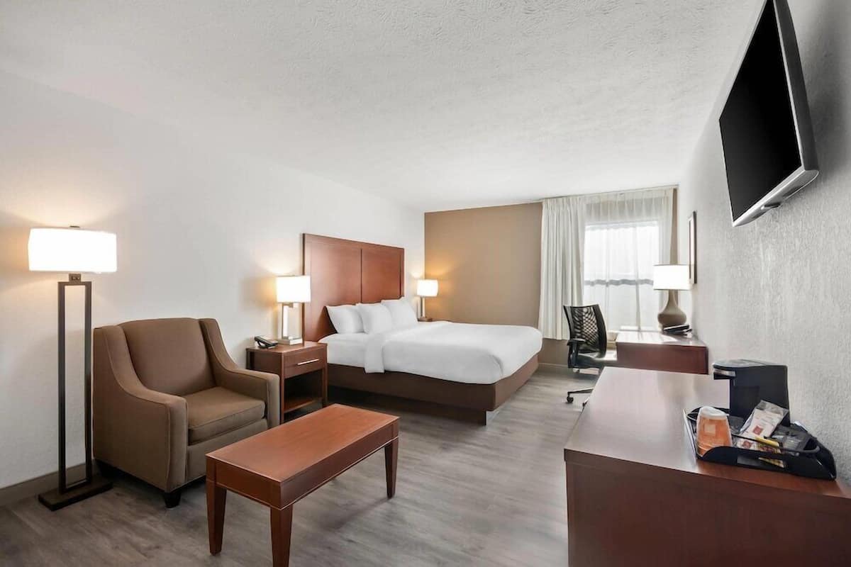 A hotel room with a bed, a desk, a chair, a lamp, and a TV.