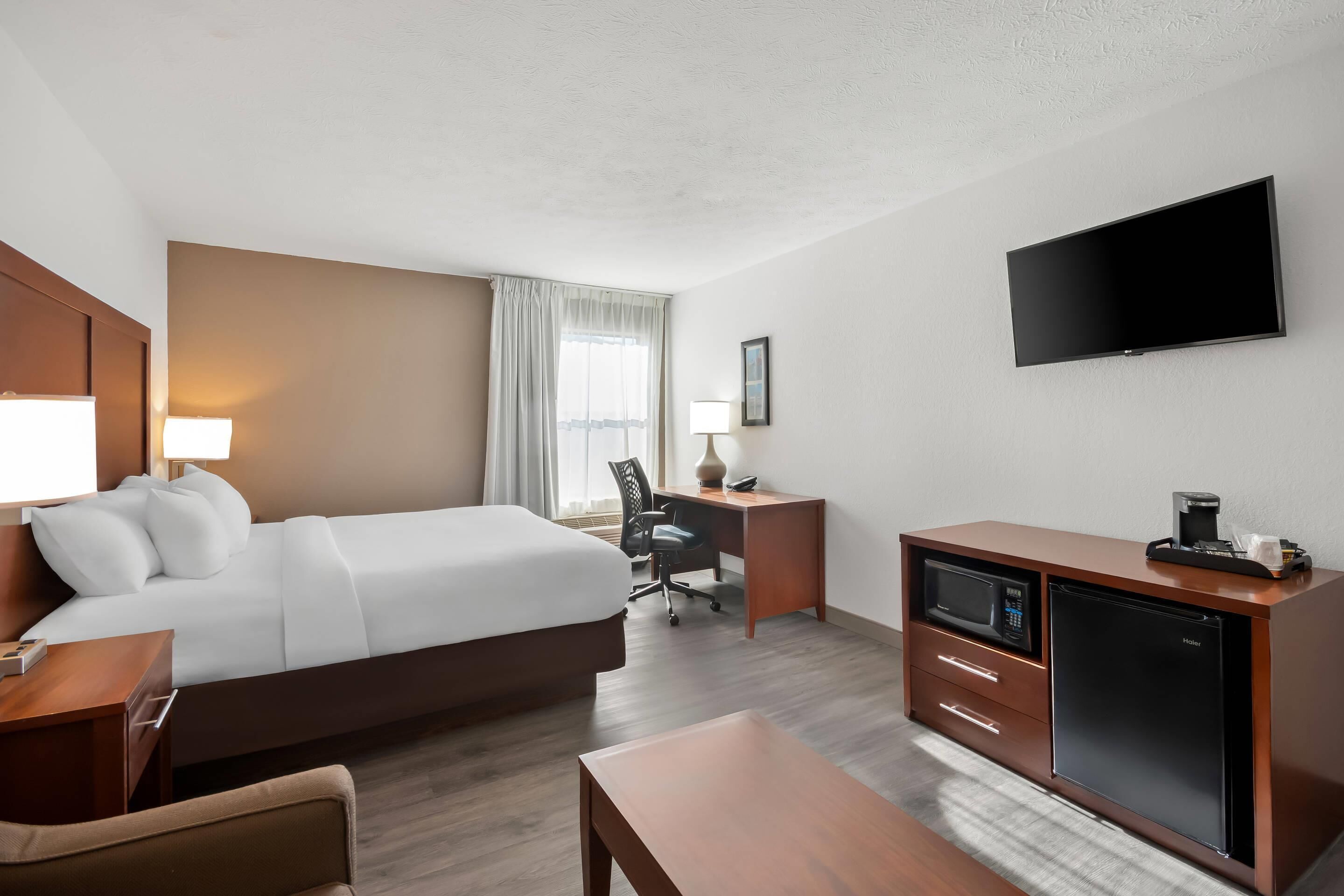 Una habitación de hotel con cama, escritorio, televisión y un minibar.