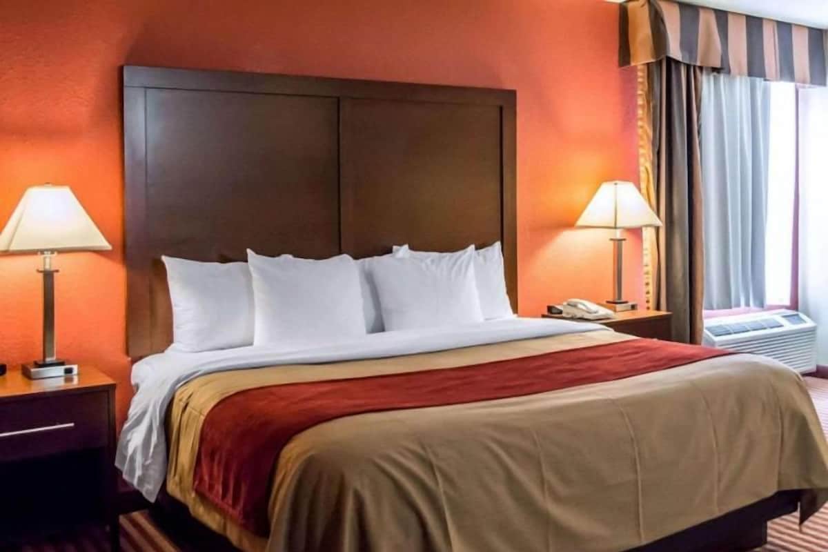 A hotel room with a large bed, two bedside lamps, a telephone, and a window with curtains.