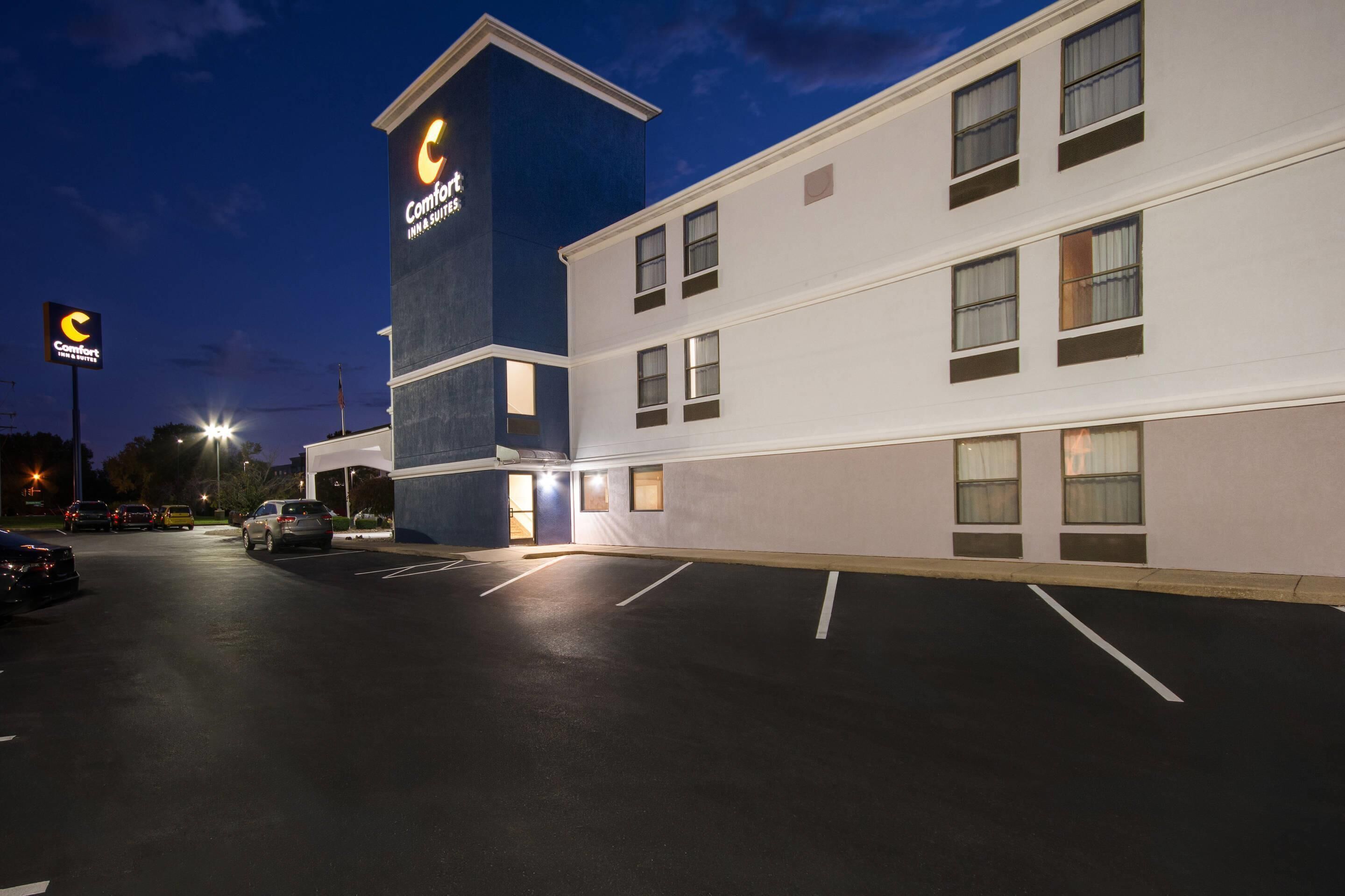 A Comfort Inn & Suites hotel with a modern design, featuring a prominent tower with signage, a parking lot with marked spaces, and a well-lit facade.