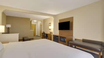 A hotel room with a large bed, a desk with a lamp, a television mounted on the wall, and a bench.