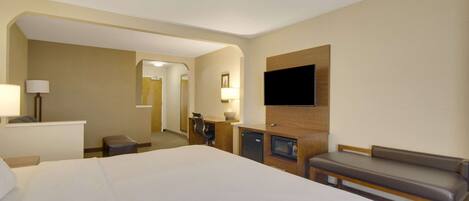 A hotel room with a large bed, a desk with a lamp, a television mounted on the wall, and a bench.