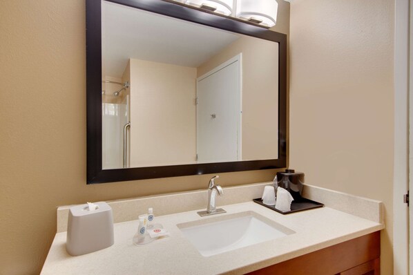A hotel bathroom with a large mirror, a sink, a towel dispenser, and a coffee maker.