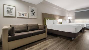 A hotel room with a sofa, a bed with white linens, a headboard, and framed artwork on the wall.