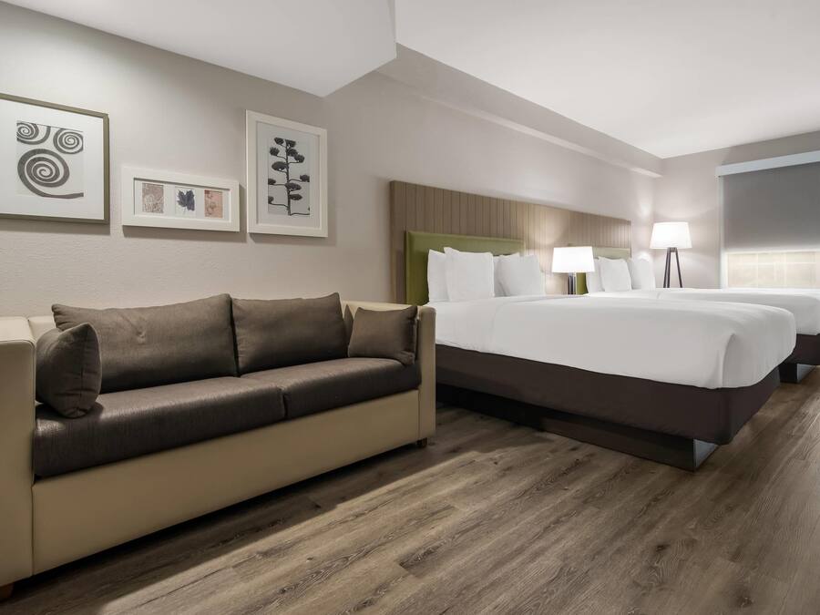 A hotel room with a sofa, a bed with white linens, a headboard, and framed artwork on the wall.