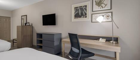 A hotel room with a bed, a desk with a chair, a TV, and artwork on the wall.
