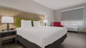 A hotel room with a large bed, two bedside tables with lamps, a red chair, and a window with blinds.