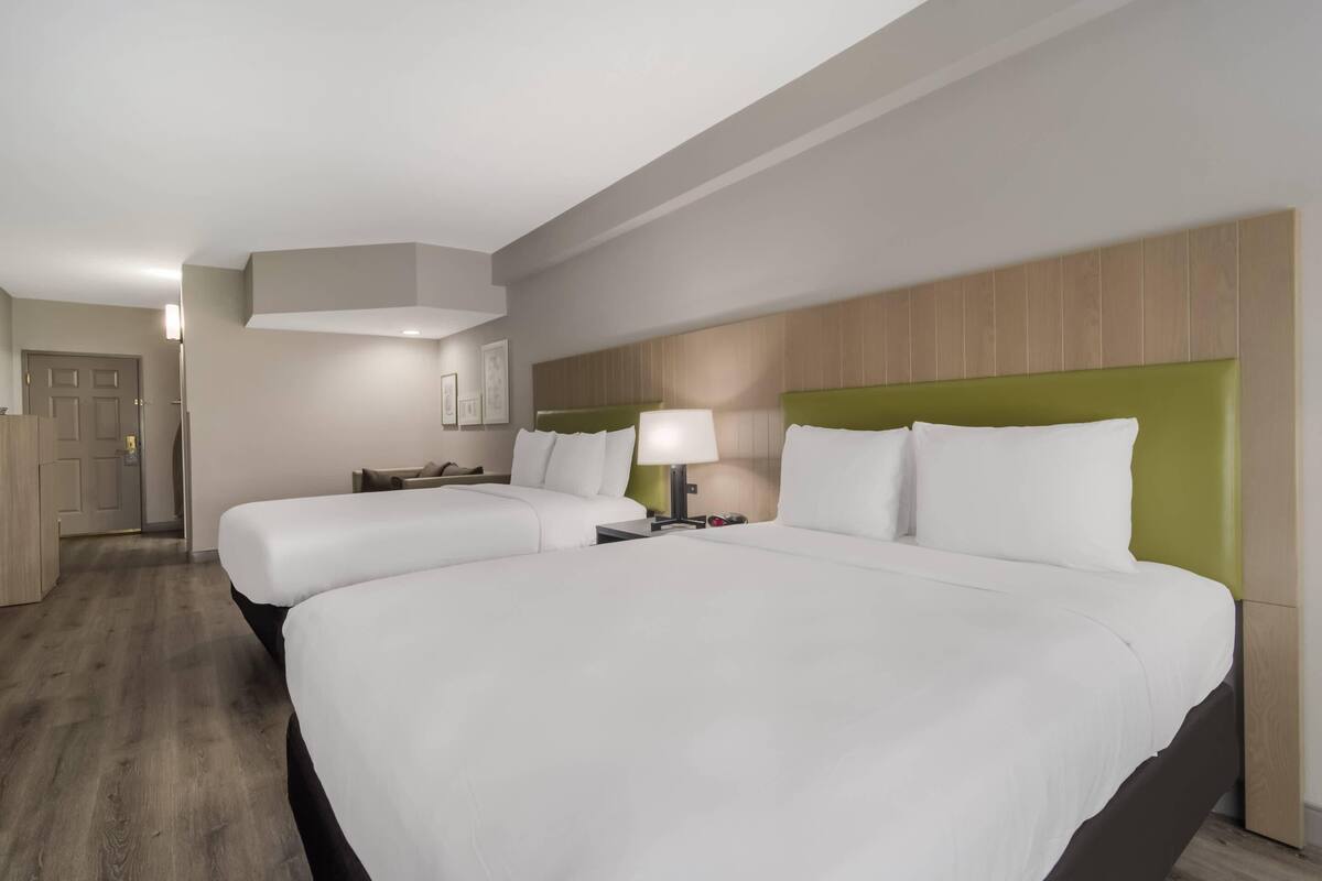 Ein Hotelzimmer mit zwei Betten, einem Holz-Kopfteil, einem Nachttisch mit Lampe und Holzboden.