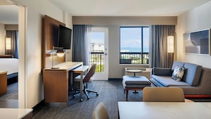 Habitación de hotel con cama, escritorio, silla, sofá y un amplio ventanal con vistas a la ciudad.