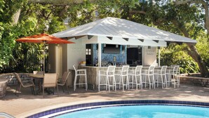 Zona de bar junto a la piscina con área de estar cubierta, piscina y pared de piedra.