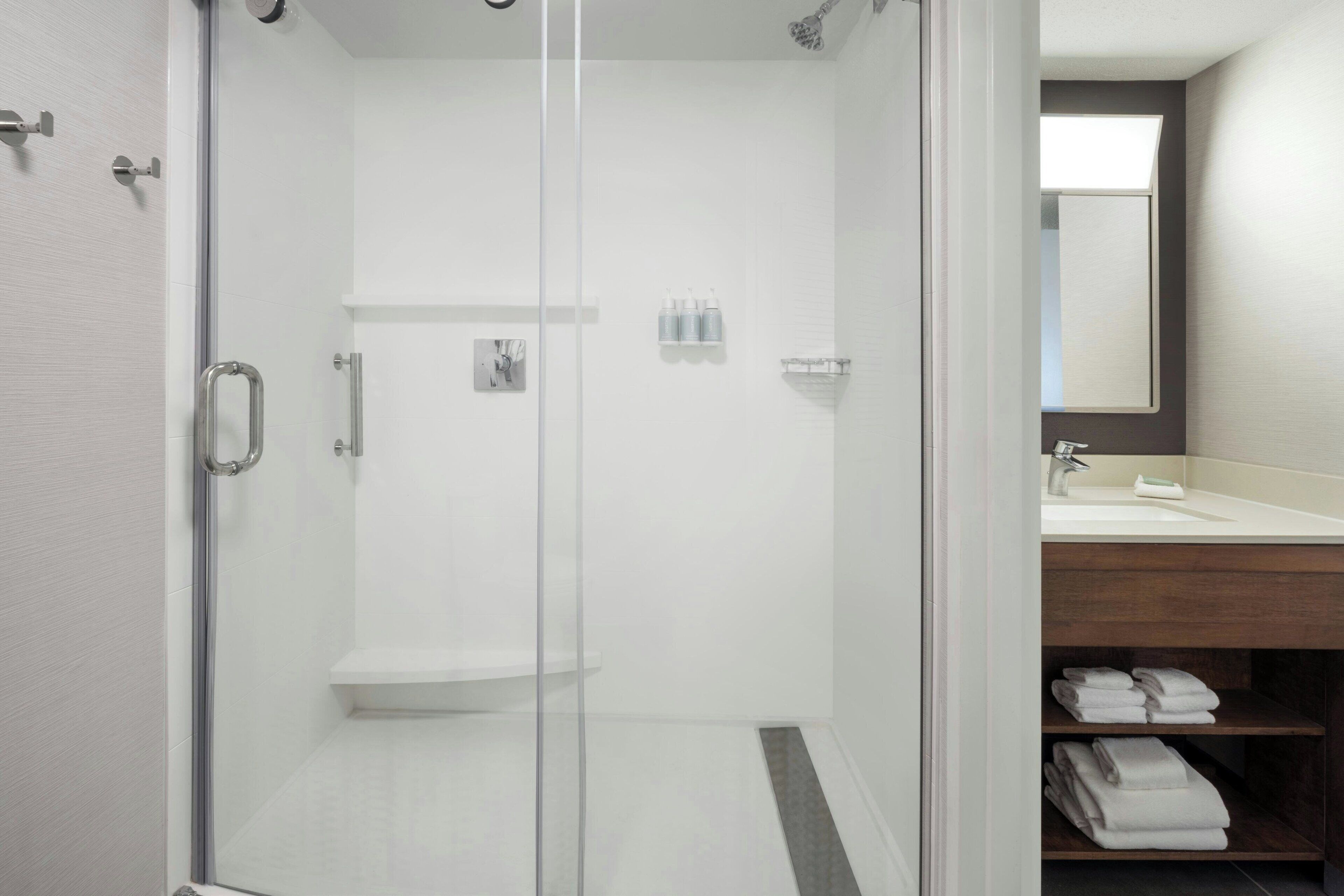 Un baño moderno con ducha de vidrio, tocador de madera con espejo y toallas ordenadamente dobladas.