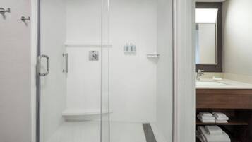 Un baño moderno con ducha de vidrio, tocador de madera con espejo y toallas ordenadamente dobladas.