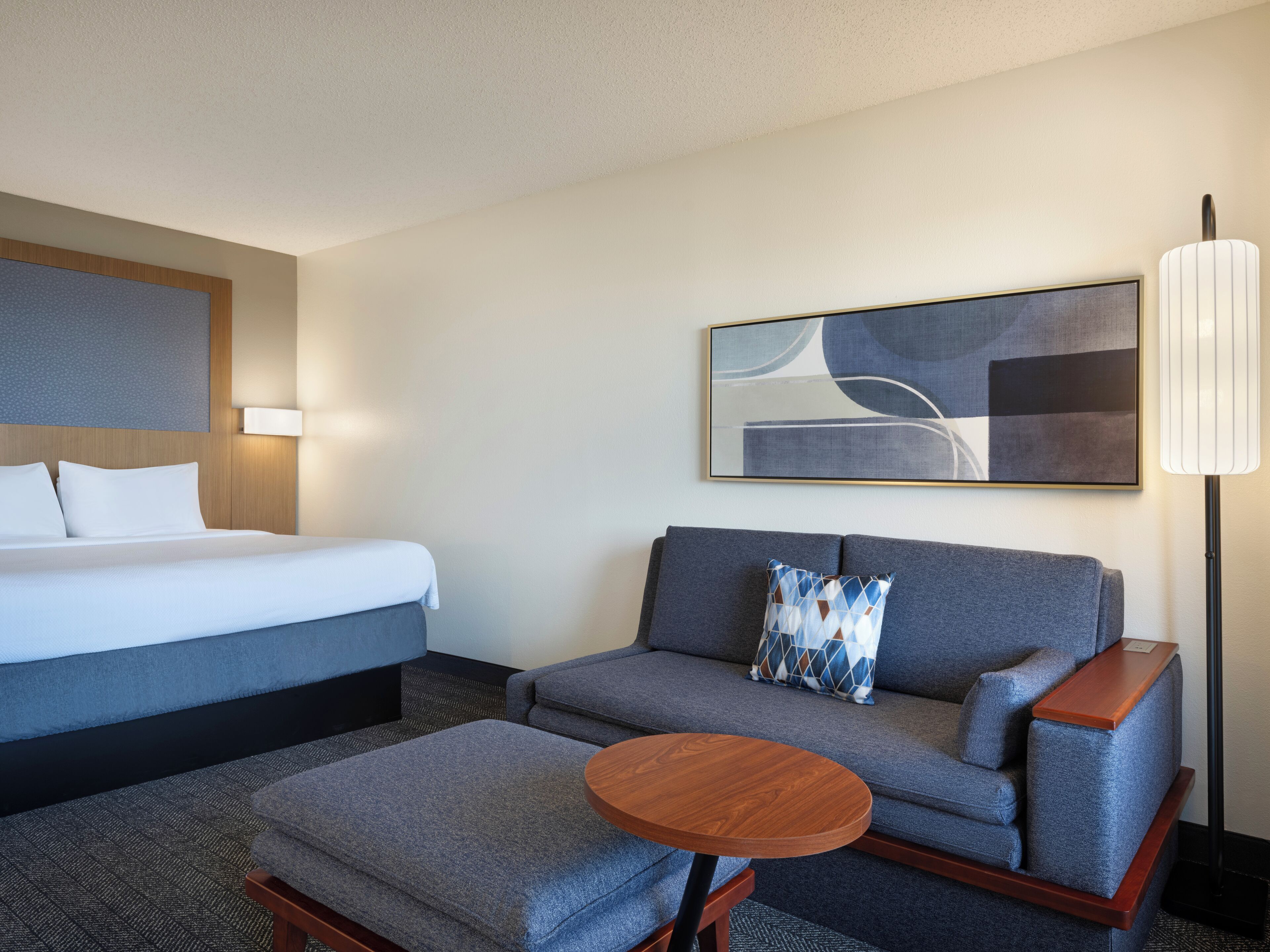 Une chambre d’hôtel avec un lit, un canapé, une petite table et une lampe.