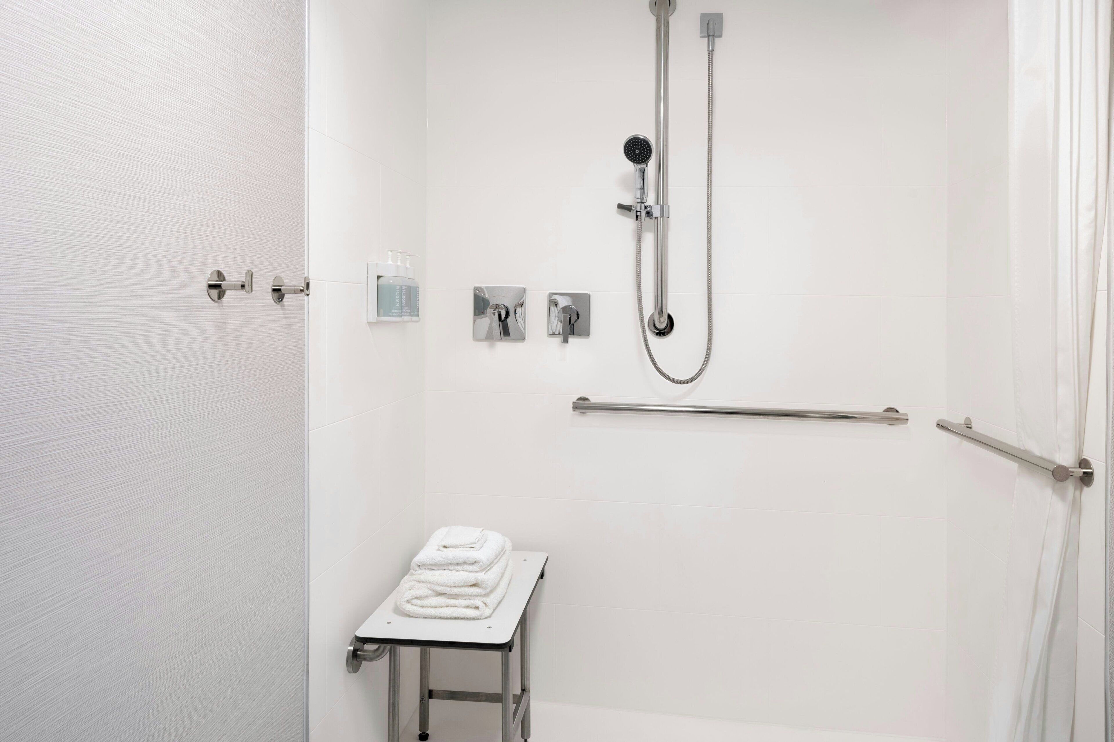 A modern bathroom with a walk-in shower, a towel rack, and a small table with folded towels.