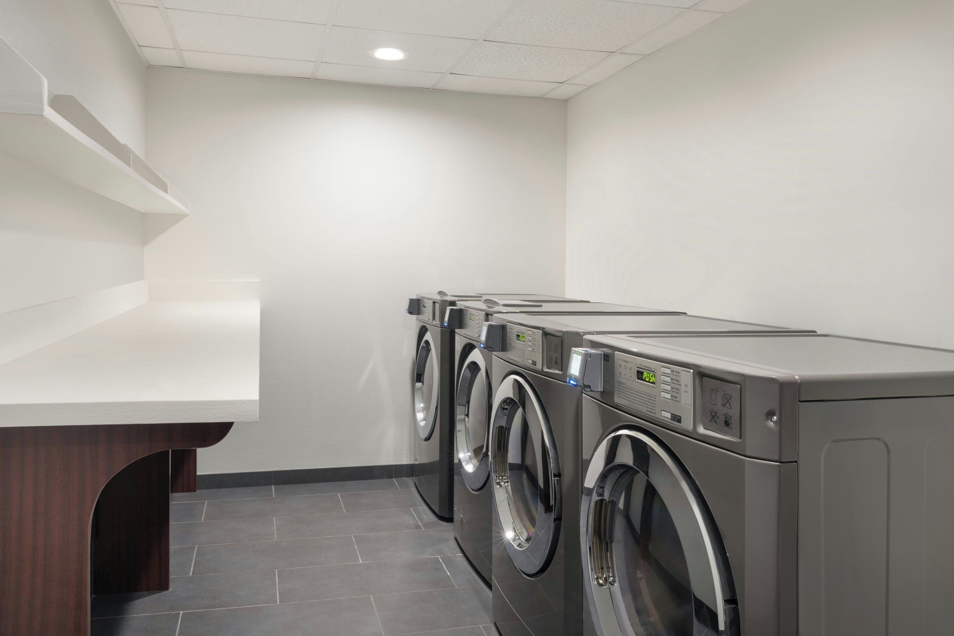 A laundry room with three stacked front-loading washers and dryers, a wooden counter, and a tiled floor.