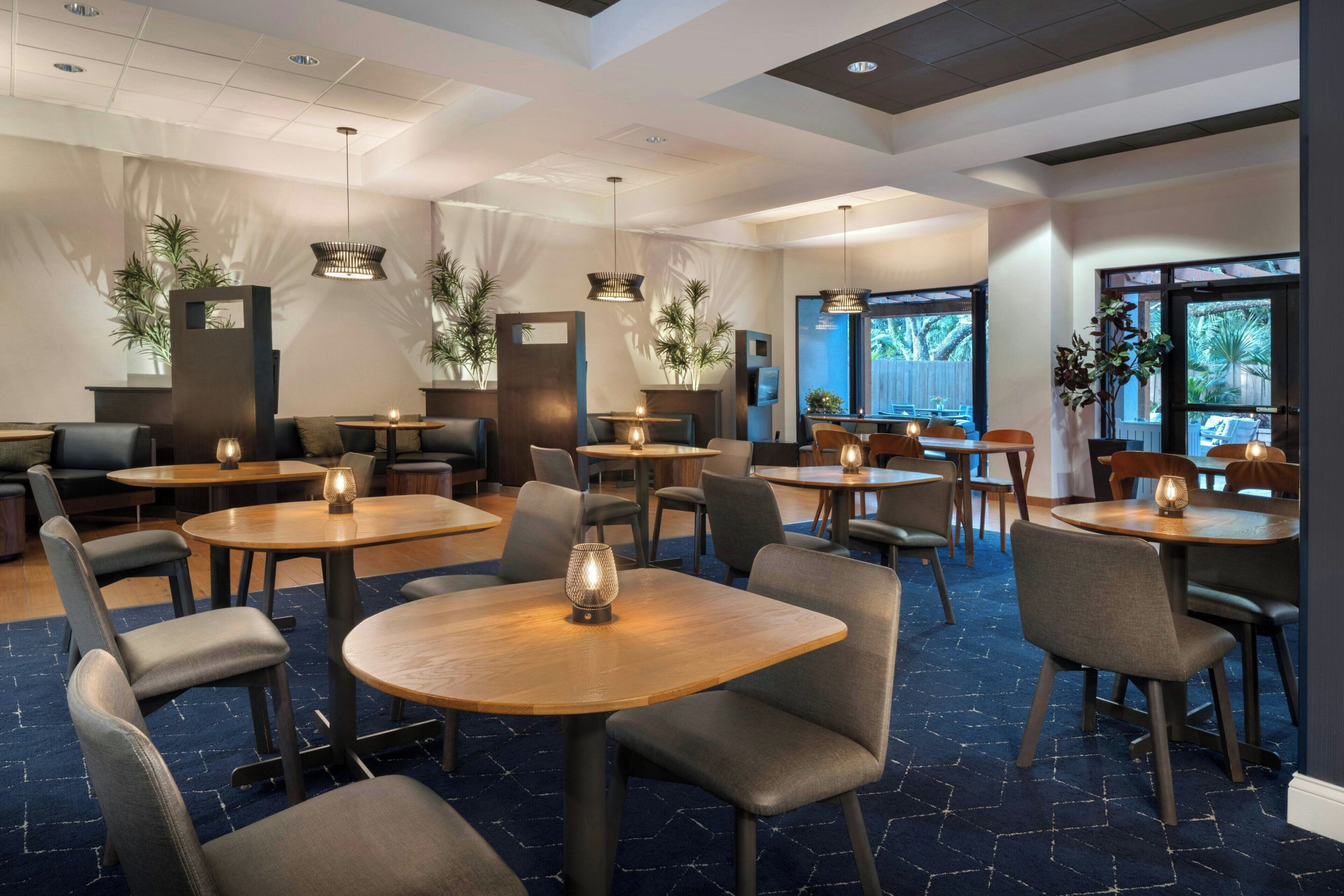 Ein Hotelrestaurant mit runden Tischen, Stühlen und Pendelleuchten.