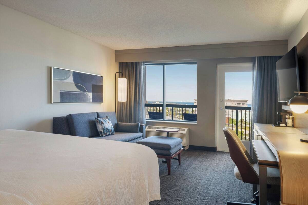 Habitación de hotel con una cama grande, un escritorio, una silla, un sofá y vistas a la ciudad desde la ventana.