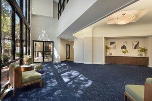 A spacious lobby with a high ceiling, large windows, and a dark patterned carpet. - Courtyard Cocoa Beach Cape Canaveral (Cocoa Beach)