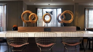 A modern dining area with a long table, three wireframe chairs, and a decorative wooden sculpture.