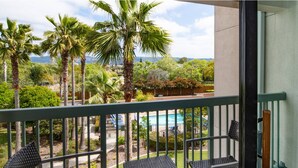 A balcony with two chairs and a table, overlooking a pool and palm trees.