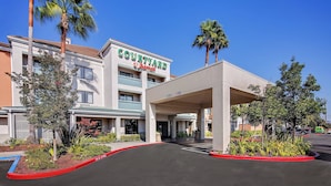 A Courtyard by Marriott hotel with a covered entrance, palm trees, and a landscaped garden.