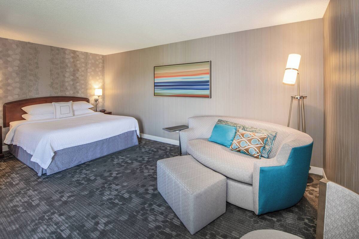 Una habitación de hotel con cama, sofá, una mesita y una lámpara de pie.