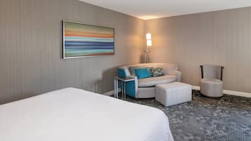 A hotel room with a large bed, a sofa, a chair, and a floor lamp.