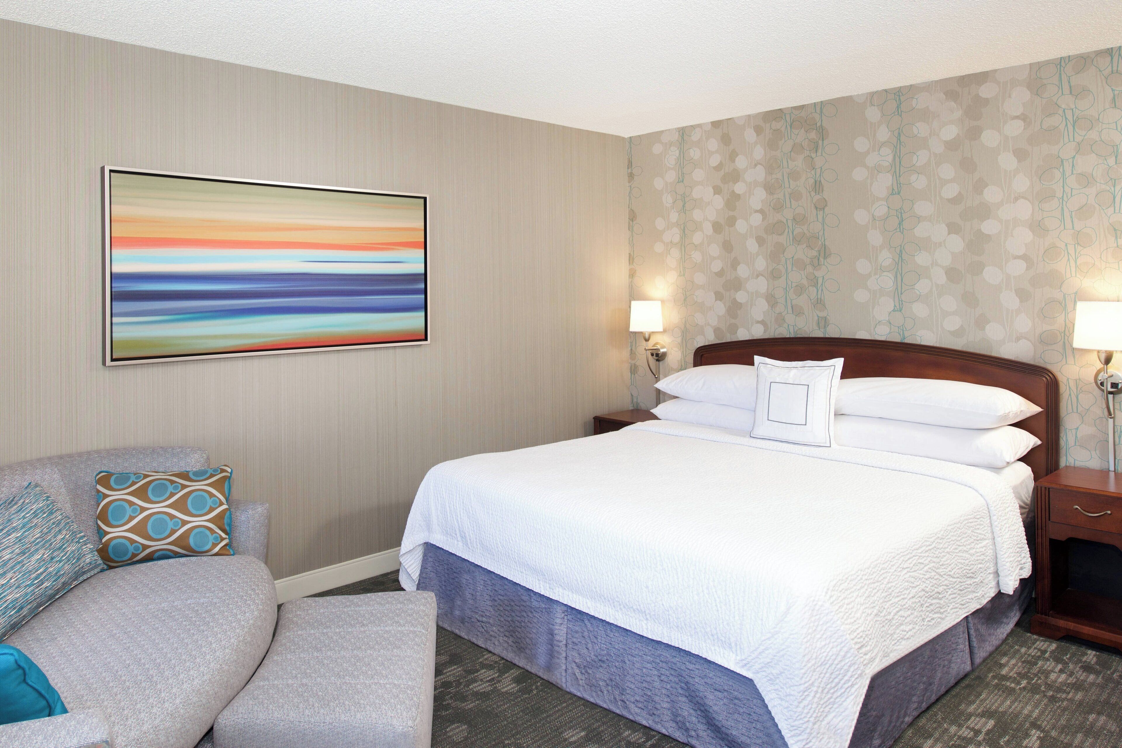 A hotel room with a large bed, a sofa, two bedside tables with lamps, and a wall with a floral wallpaper pattern.