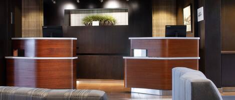 A reception area with two wooden reception desks, a seating area with upholstered chairs, and a potted plant on the wall.