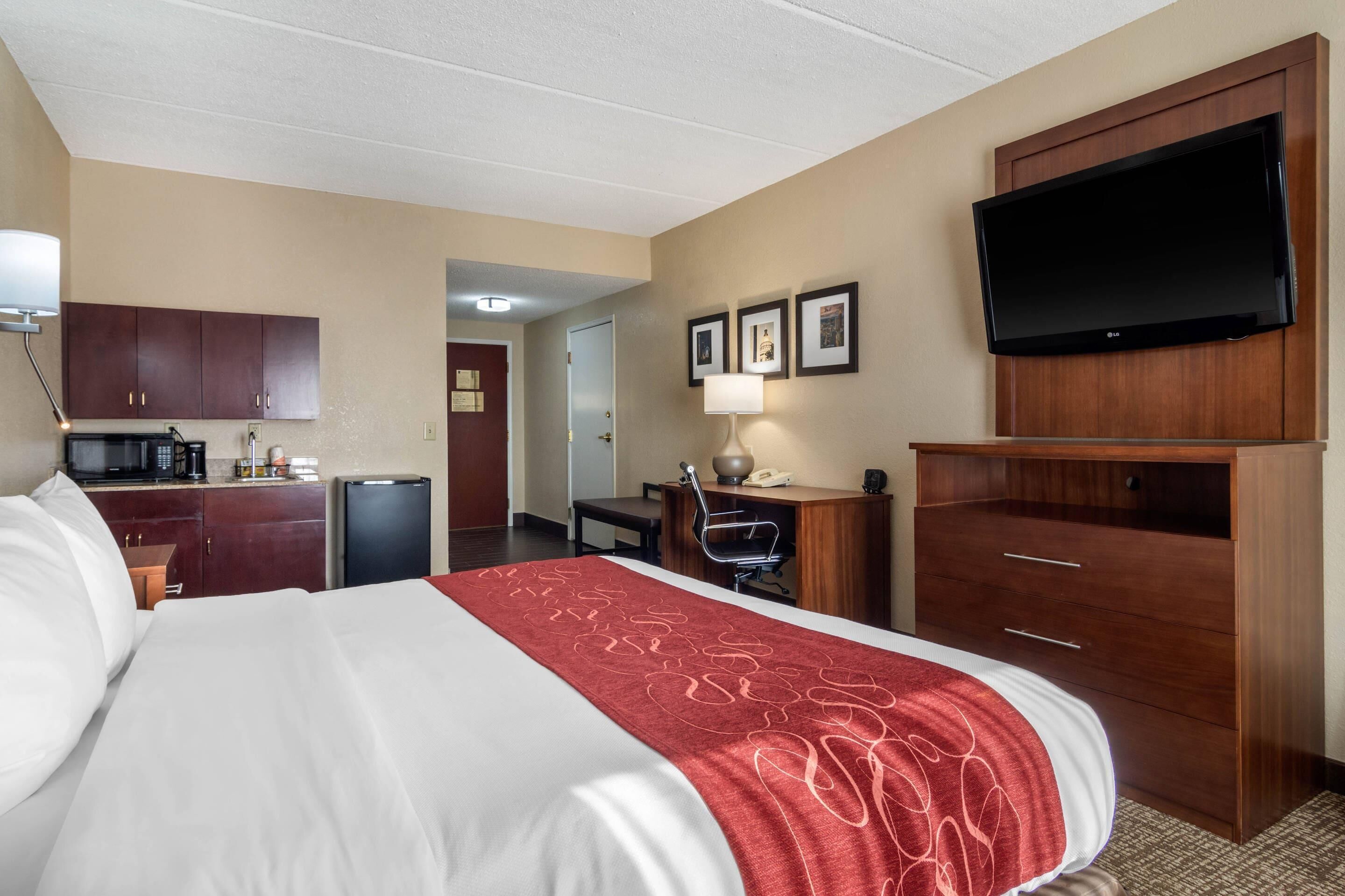 Una habitación de hotel con cama, escritorio, televisión y kitchenette.