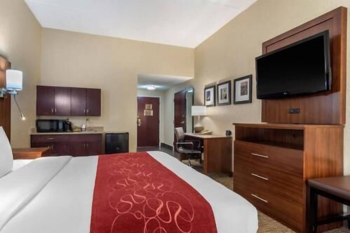 A hotel room with a bed, a desk, a television, and a kitchenette.