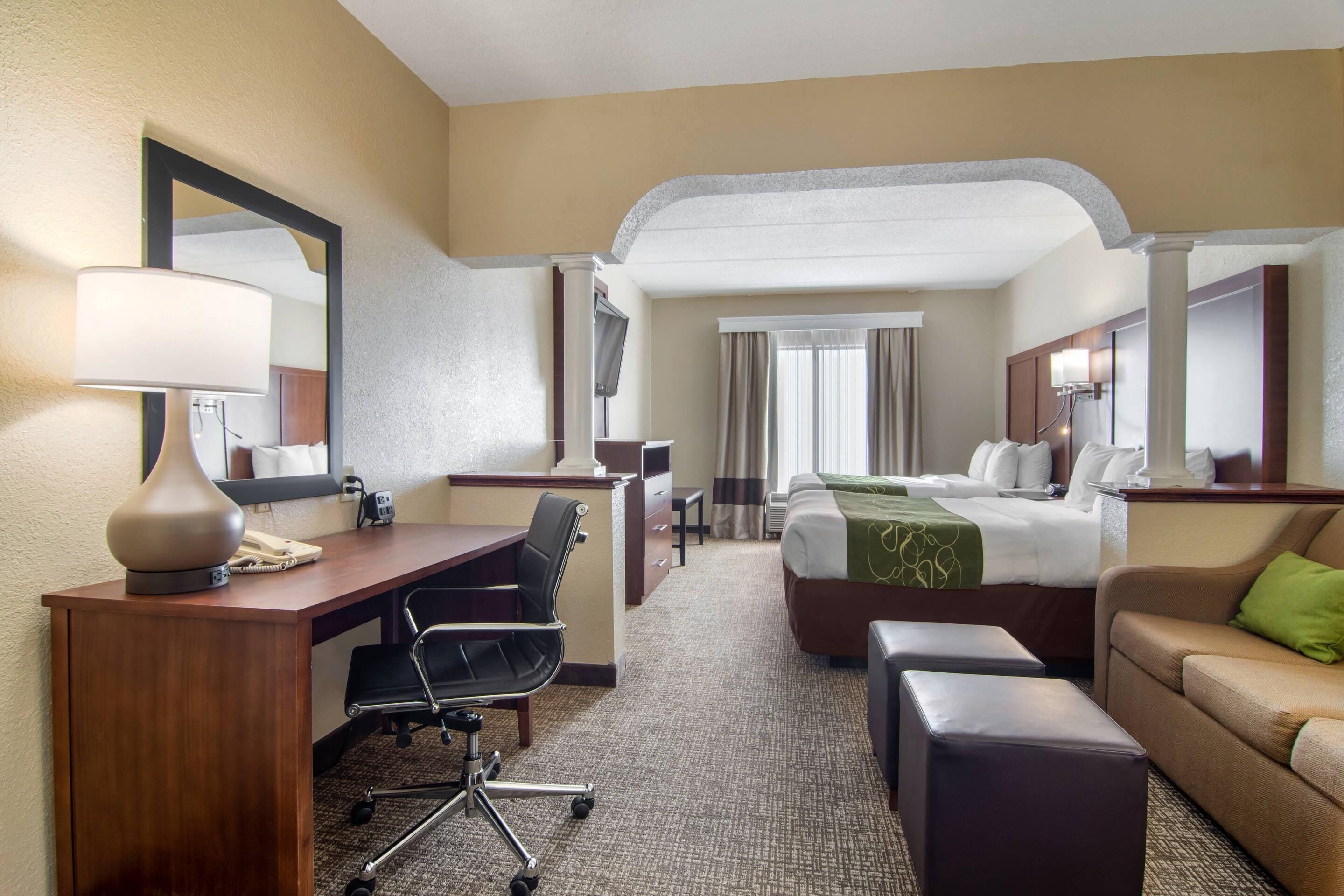 A hotel room with a desk, chair, bed, and a sofa.