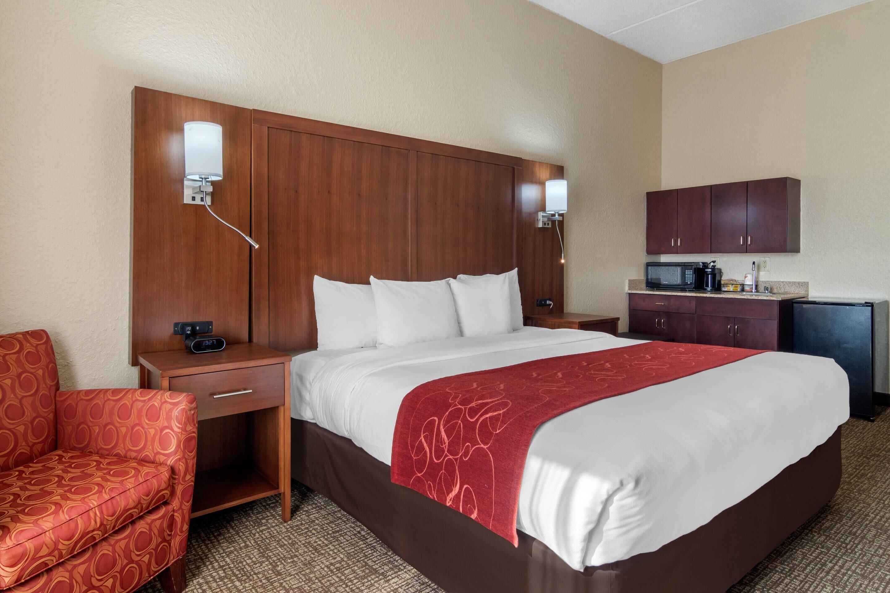 A hotel room with a large bed, a desk with a telephone, a chair, a microwave, and a small refrigerator.
