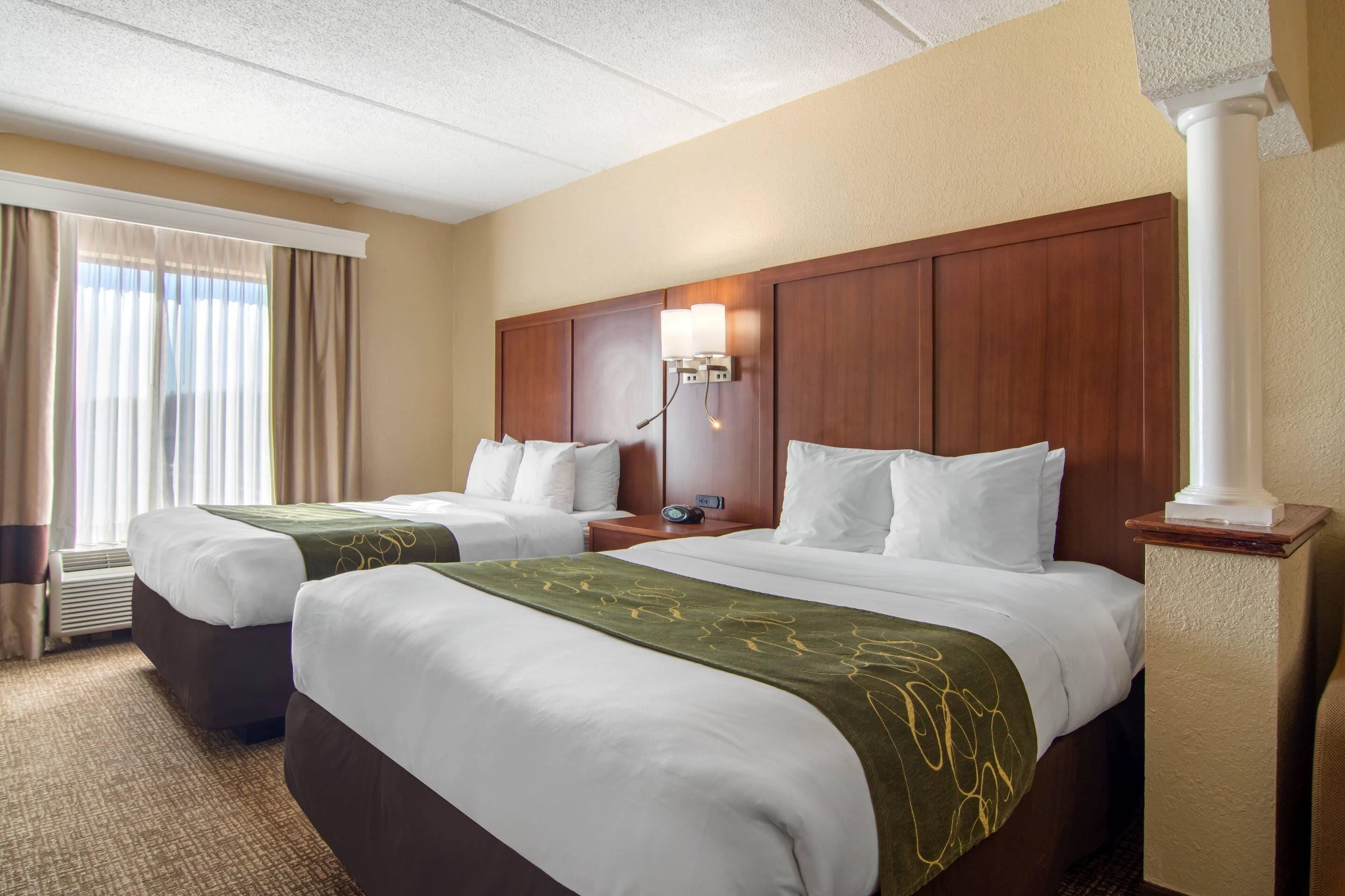 A hotel room with two beds, a nightstand, a lamp, and a window with curtains.