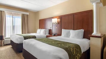 A hotel room with two beds, a nightstand, a lamp, and a window with curtains.