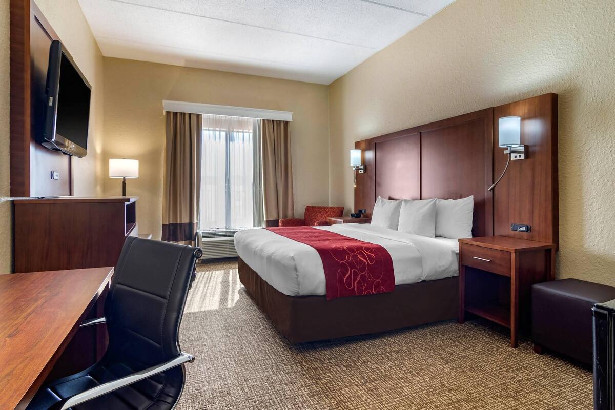 A hotel room with a bed, desk, chair, TV, and a window with curtains.