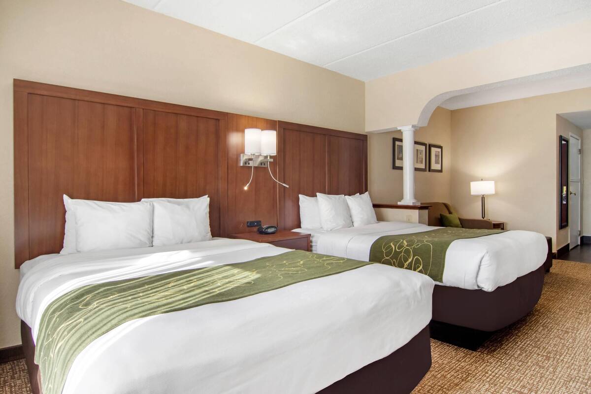 A hotel room with two beds, a wooden headboard, bedside lamps, and a carpeted floor.